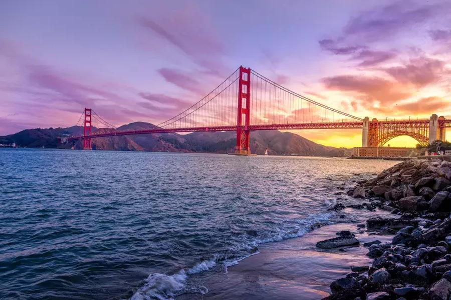 Die 金门大桥 bei Sonnenuntergang mit einem bunten Himmel und der San Francisco Bay im Vordergrund.